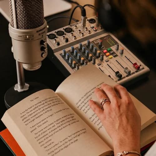 A studio microphone and mixing desk beside an open book